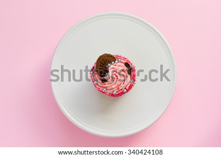 Pink decorated cupcake on white and pink background, top view, minimal style.