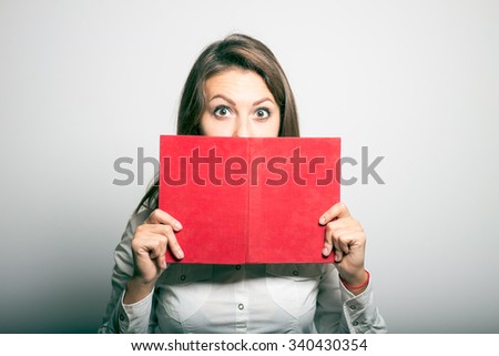 student girl hides behind the book. office manager. studio photo on a gray background