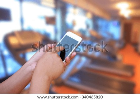 hand hold and touch screen smart phone, on abstract blur photo modern fitness center background