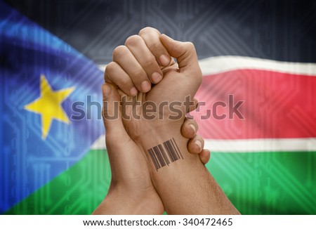 Barcode ID number tattoo on wrist of dark skinned person and national flag on background - South Sudan