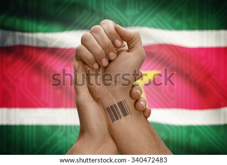 Barcode ID number tattoo on wrist of dark skinned person and national flag on background - Suriname