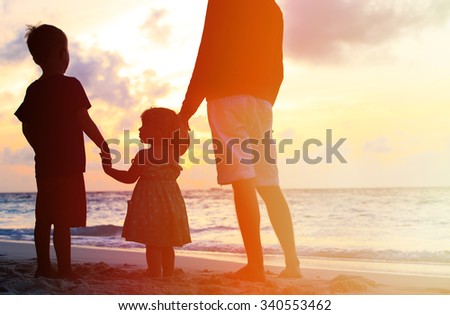 silhouette of father and two kids walking on beach at sunset