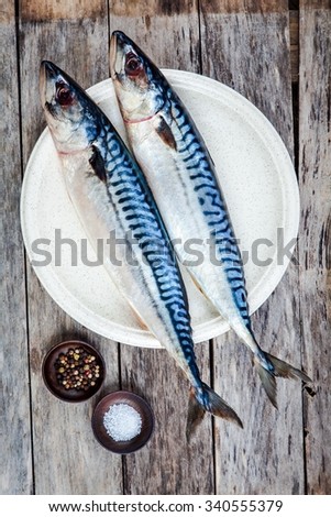 Two raw fresh mackerel fishes on a plate with salt and pepper on wooden table