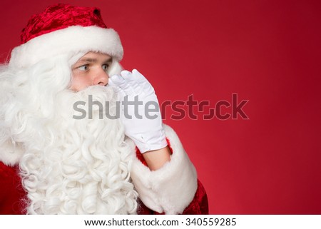 Hey I have got something for you. Closeup profile of Santa Claus whispering to the blank copyspace on red background