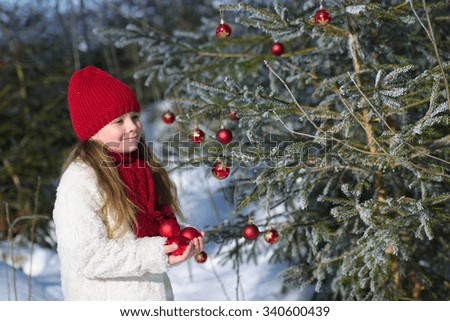 Smiling girl holding Christmas baubles in hands in winter forest