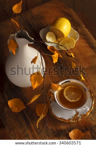 Cup of hot tea, lemons and jug of birch branch on rough wooden surface. Beautiful autumn still life. Top view. 