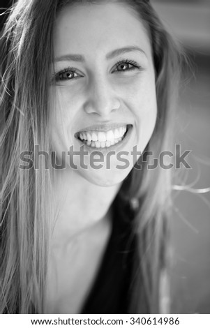 Closeup portrait of one beautiful happy smiling blonde young woman with long hair outdoor looking forward on blurred background black and white, vertical picture