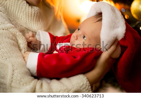 Closeup photo of mother holding baby boy in Santa costume and hat