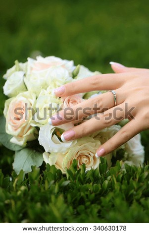 Closeup view of one big round beautiful fresh wedding bouquet of rose flowers pink white and yellow pastel colors lying on green grass sunny day outdoor with female hand, vertical picture