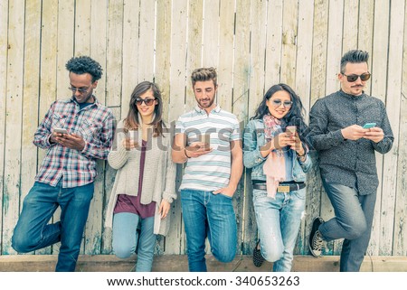 Young people looking down at cellular phone - Teenagers leaning on a wall and texting with their smartphones - Concepts about technology and global communication Royalty-Free Stock Photo #340653263