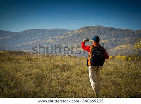 Male tourist with backpack taking pictures of the autumn scenery to your smartphone.
