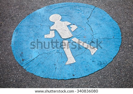 Pedestrian lane road marking, white schematic walking man in blue circle over rough asphalt pavement