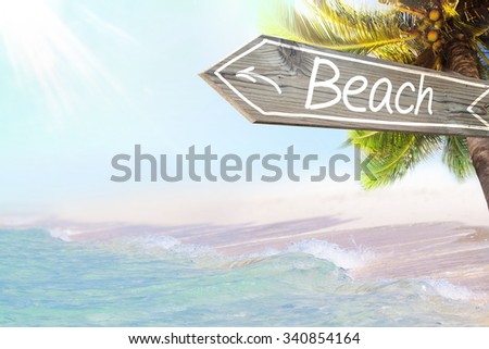 Beach wooden sign and blurry exotic beach background. Tropical landscape with coconut palm tree and white sand beach. Paradise design banner background.