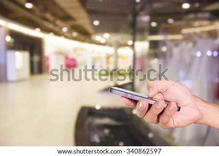 Mobile hold in hand with blur shopping mall