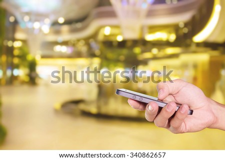 Mobile hold in hand with blur shopping mall
