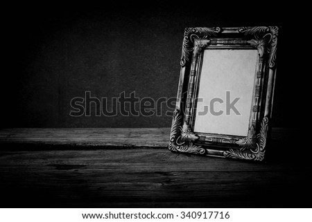 Vintage photo frame on wooden table over grunge background, black and white