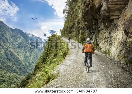 Bike adventure travel photo. Bike tourists  ride on the "road of death"  downhill track  in Bolivia. In the background sky circles a condor over the scene. Royalty-Free Stock Photo #340984787