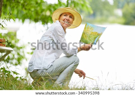 Old happy woman painting a picture with brush in nature
