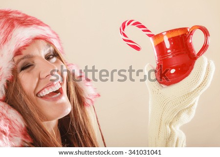 Young woman holding xmas mug with candy cane. Girls hands in woolen white gloves winked. Christmas time concept.
