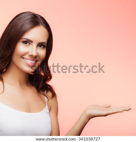Portrait of cheerful smiling young woman showing copyspace or something, over blue background