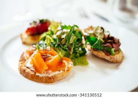 Plate of assorted Italian appetizer bruschetta with chopped vegetables, salmon and meat on ciabatta bread, garnished with green mix salad Royalty-Free Stock Photo #341130512