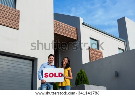 Happy couple in front of new house with sold sign