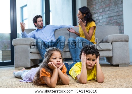 Children laying on the carpet in living room while parents arguing on the sofa Royalty-Free Stock Photo #341141810