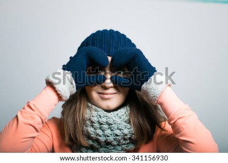 sweet girl looks to the future through hand binoculars, dressed in winter clothes. hipster, isolated on a gray background
