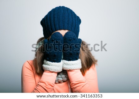 sweet girl covers her face, dressed in winter clothes. hipster, on a gray background
