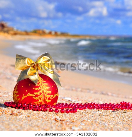 Red christmas ball with golden bow on the sand against blue ocean