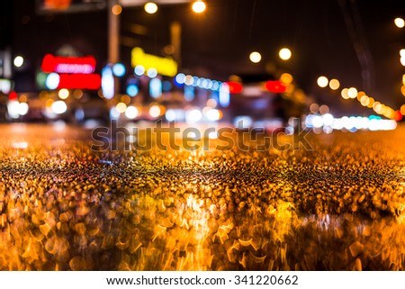 Rainy night in the big city, dense traffic at a busy intersection in the light of shop windows. View from the level of asphalt