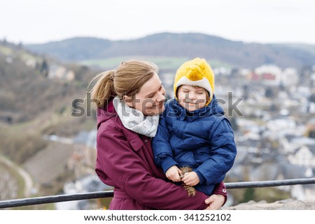Cute little child and young mother enjoying a view on european city from above. Happy family on cold autumn day, wearing warm clothes.