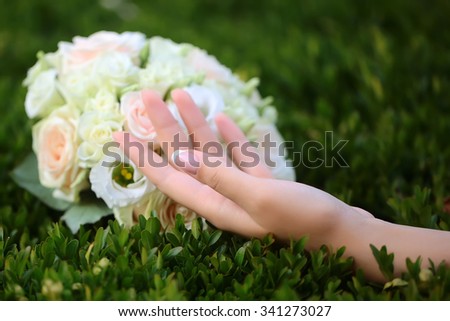 Closeup view of one big round beautiful fresh wedding bouquet of rose flowers pink white and yellow pastel colors lying on green grass sunny day outdoor with female hand, horizontal picture