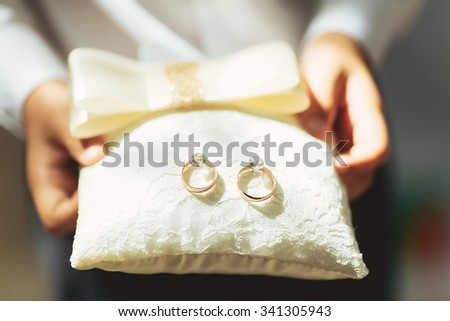 boy holds a magnificent pair of shiny golden wedding rings on a pillow Royalty-Free Stock Photo #341305943