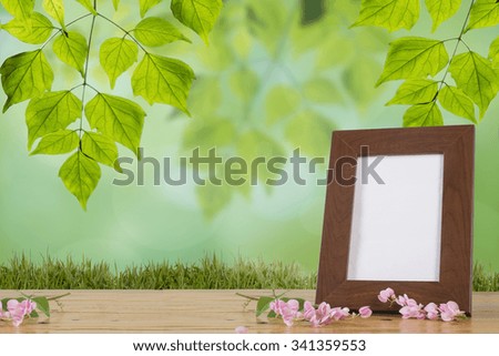 Still life with flowers and white photo frame on wooden table over nature background.