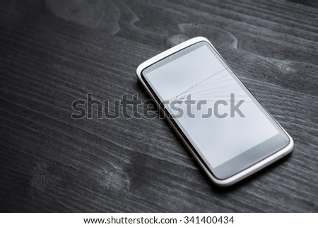 Phone display crack isolated on wooden table, broken cell phone