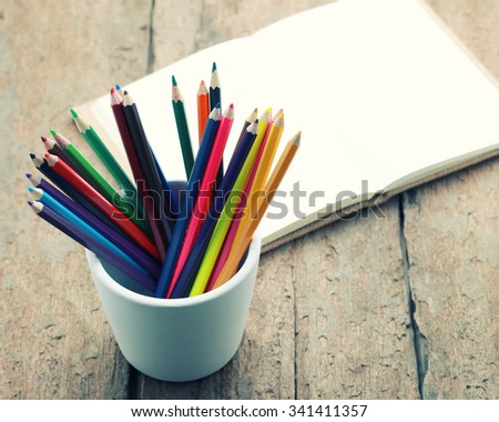 Colored pencils in cup with blank sketch book on wooden background,education concept -vintage effect.