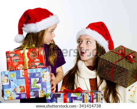 Two sisters in red sants hats with gift boxes isolated on white