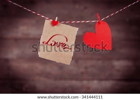 Paper hearts and sheet hanging on cord against wooden background