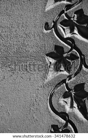 Old grave stone with ivy leaves pattern. Aged photo. Black and white.