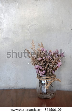 Dried flowers in glass jar on a wood table with stucco wall background