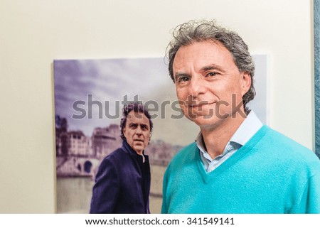 A smiling Caucasian man is looking at a photo of himself with opposite feeling