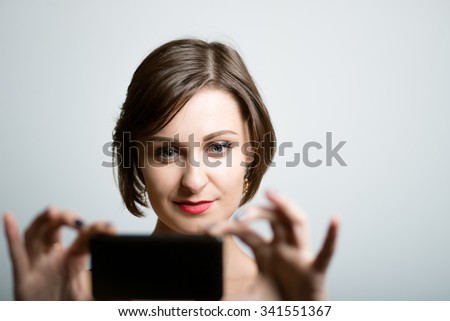 Pretty slim girl photographed on a mobile phone photo studio on isolated gray background