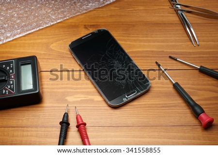 Broken smartphone with tools on table in wood