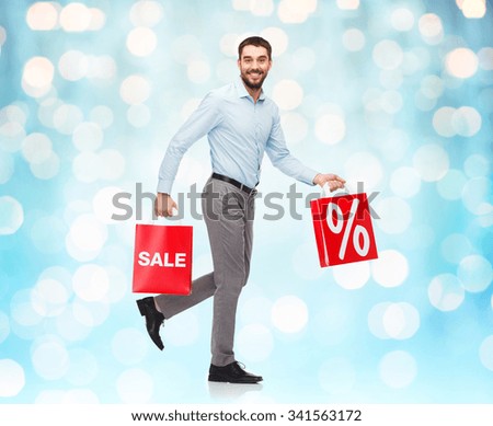 people, sale, discount and christmas concept - smiling man walking with red shopping bags over blue holidays lights background