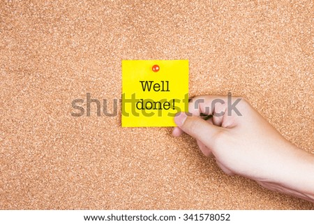 "Well done!" on a yellow sticky note on cork board with hand holding