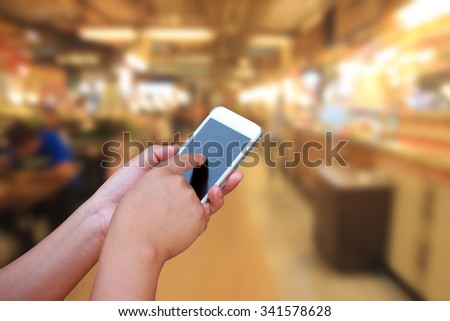 hand hold and touch screen smart phone, on blurred image people in food center with light bokeh