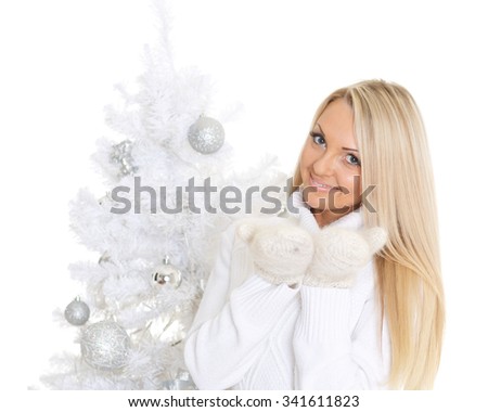 Young happy woman in winter clothes stands near Christmas tree on a white background and holds an imaginary object in a hand. Free space for advertising of your product.