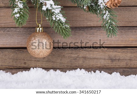 Gold Christmas bauble hanging from evergreen branch with a wood background