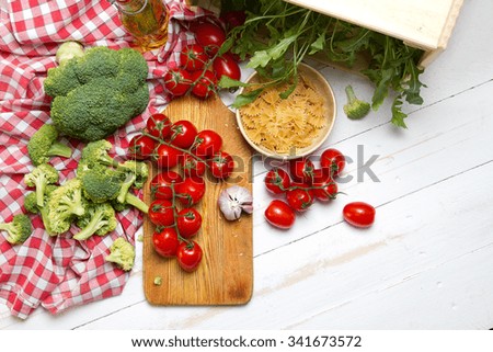Raw tomatoes, garlic, broccoli, olive oil, arugula and pasta on a white table